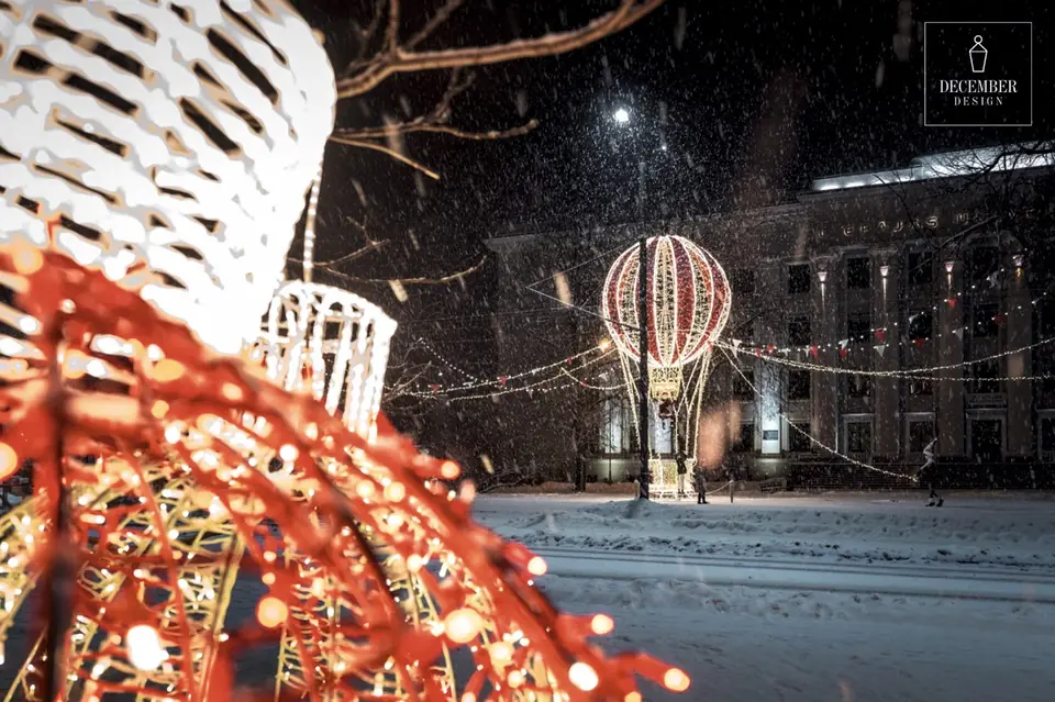 Light balloon in the snowfall in the town square, red light ornament in the foreground - Liepāja
