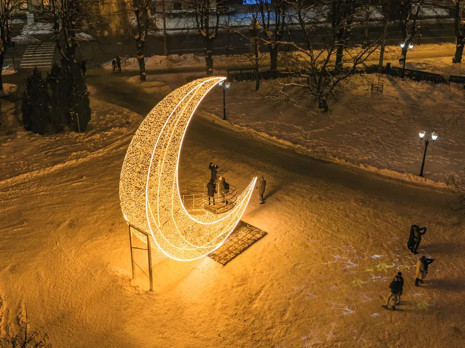 December Design izgaismota mēness instalācija sniegotā pilsētas parkā