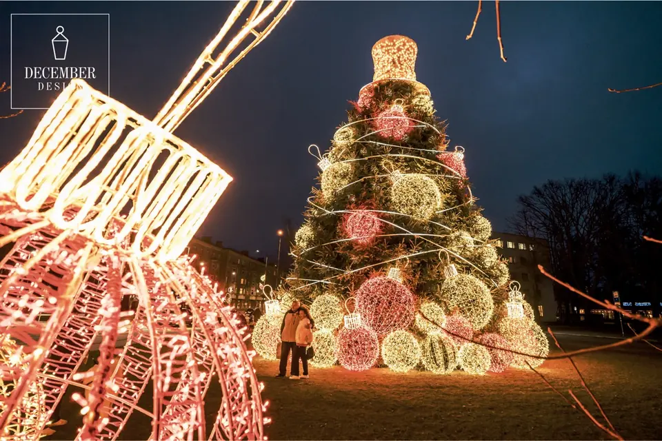 A large Christmas tree decorated with large illuminated figures of balls and lanterns, topped with a golden cylinder