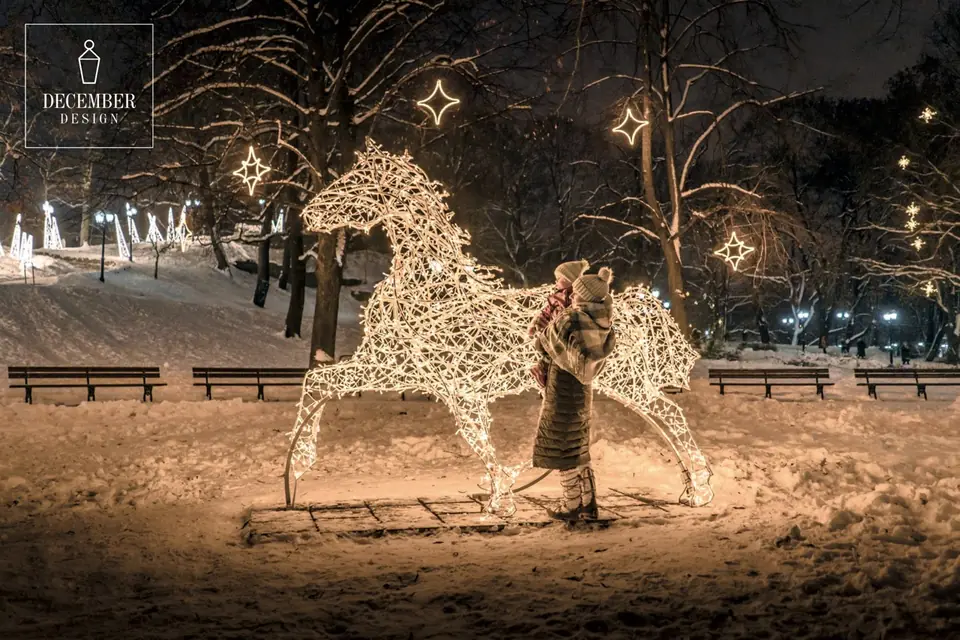 Illuminated sculpture of a horse in a snowy park - a mother and baby are standing next to it