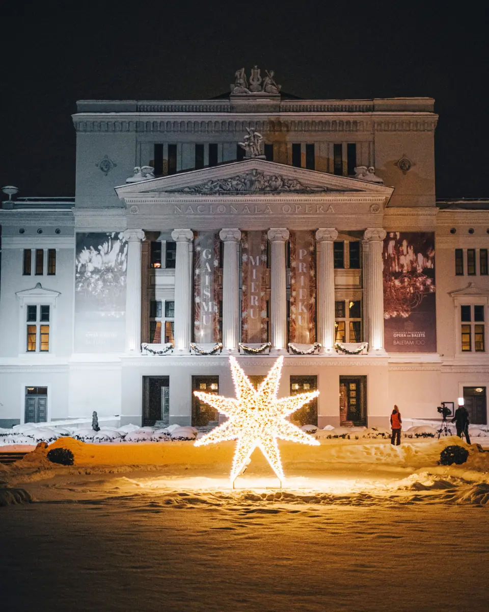 The Latvian National Opera in Riga, illuminated at night with a large light star sculpture in the foreground