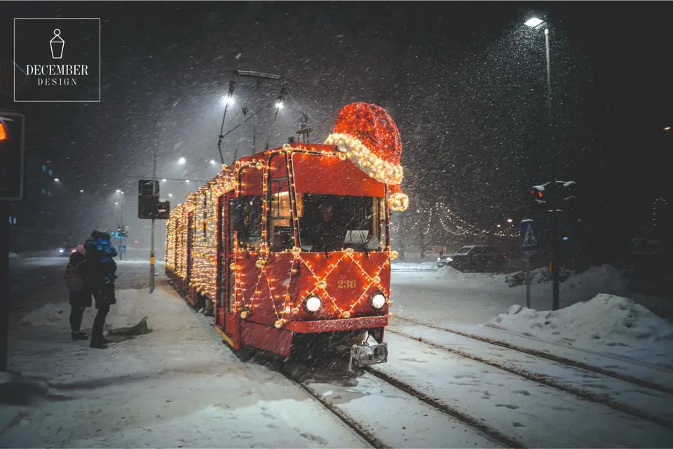 Red Christmas tram with elf hat and string lights in snowfall