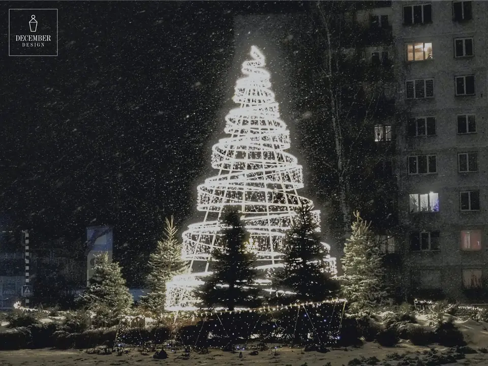 A spiral, multi-level light Christmas tree in the snow near a high-rise building during a snowfall