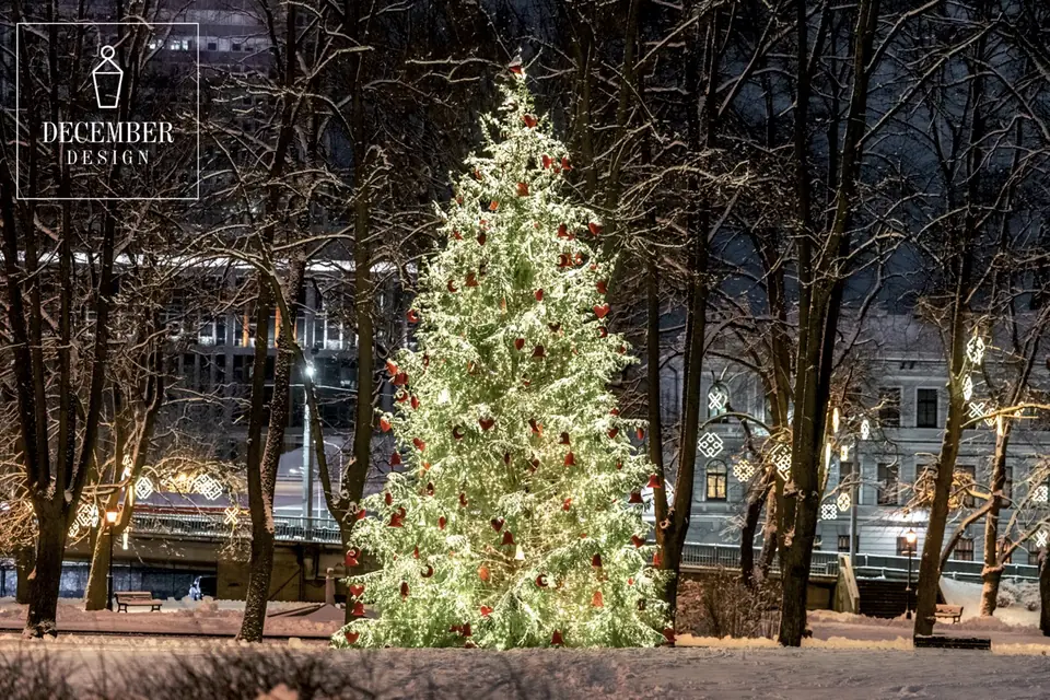A Christmas tree decorated with red balls and warm lights in a snowy park near Riga Castle