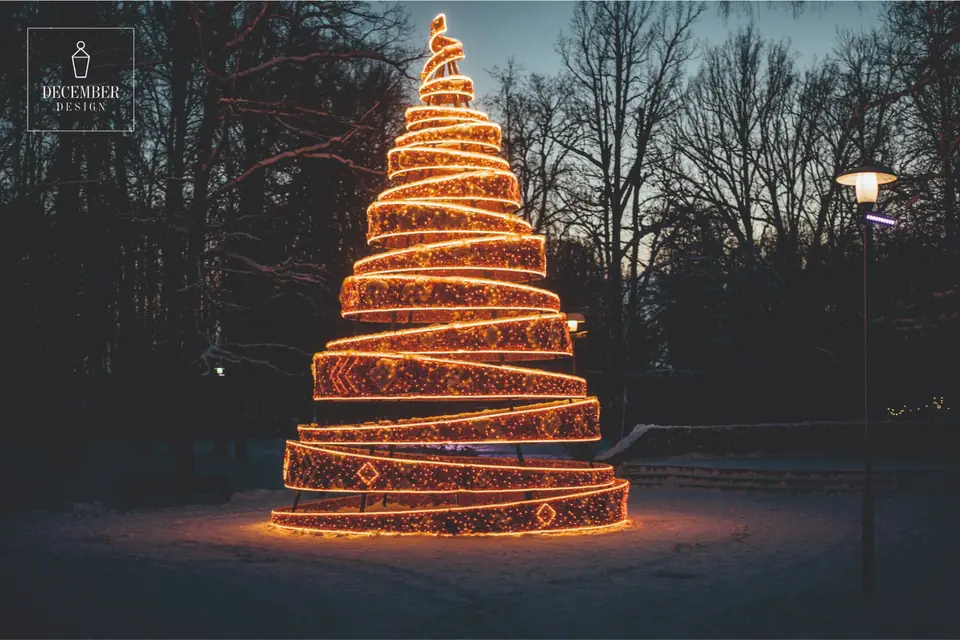 Spiral light Christmas tree with warm golden ribbons in a snowy park at dusk