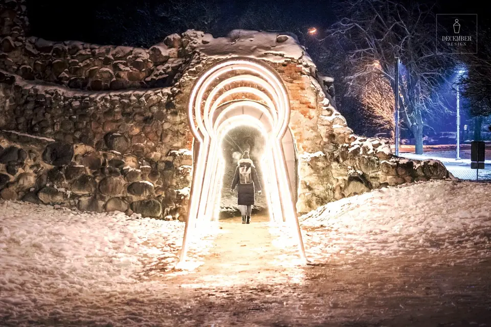 A man walks through an illuminated light tunnel in the snowy Dobele castle ruins at night