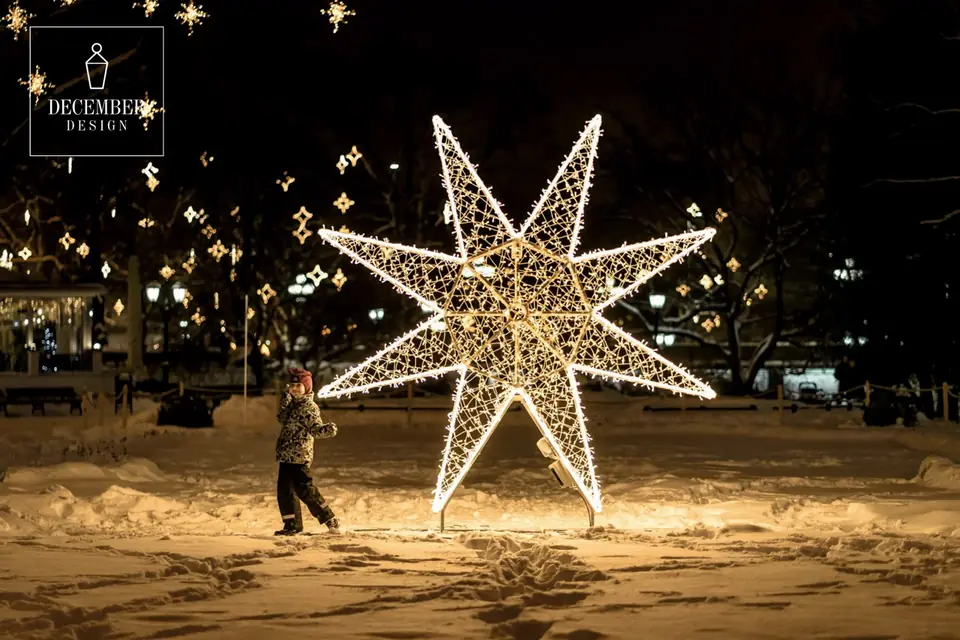 A large eight-pointed star of light in a snowy park - a child passes by it