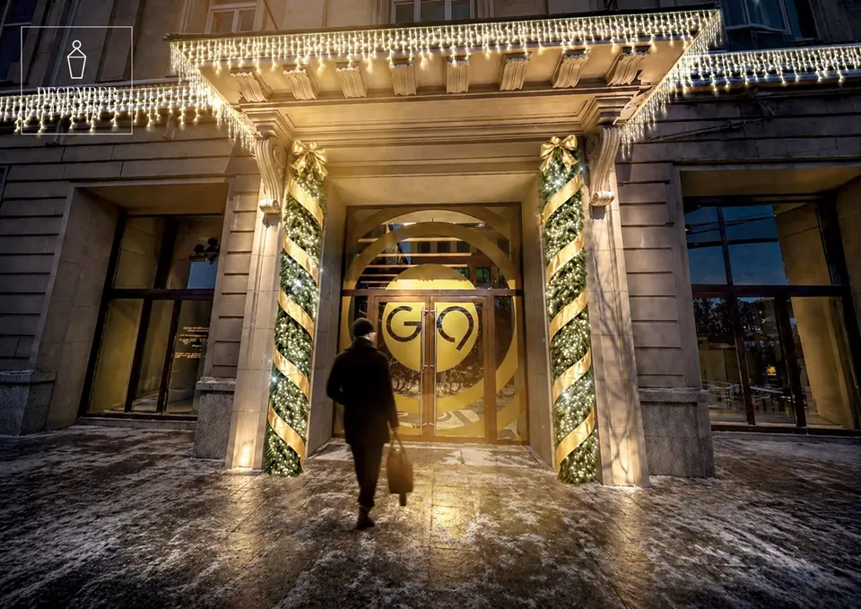 The entrance of the building with illuminated columns of greenery and gold ribbons