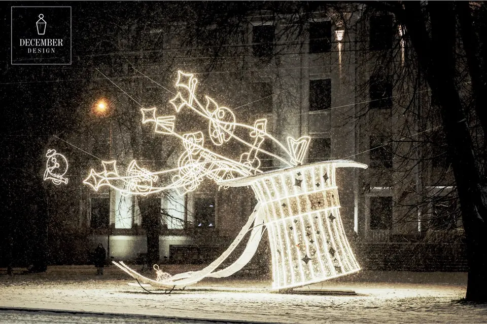 A large cylinder of light sculpture in a snowy square, from which light outlines of musical notes, a harp, a horn and a clock fall out