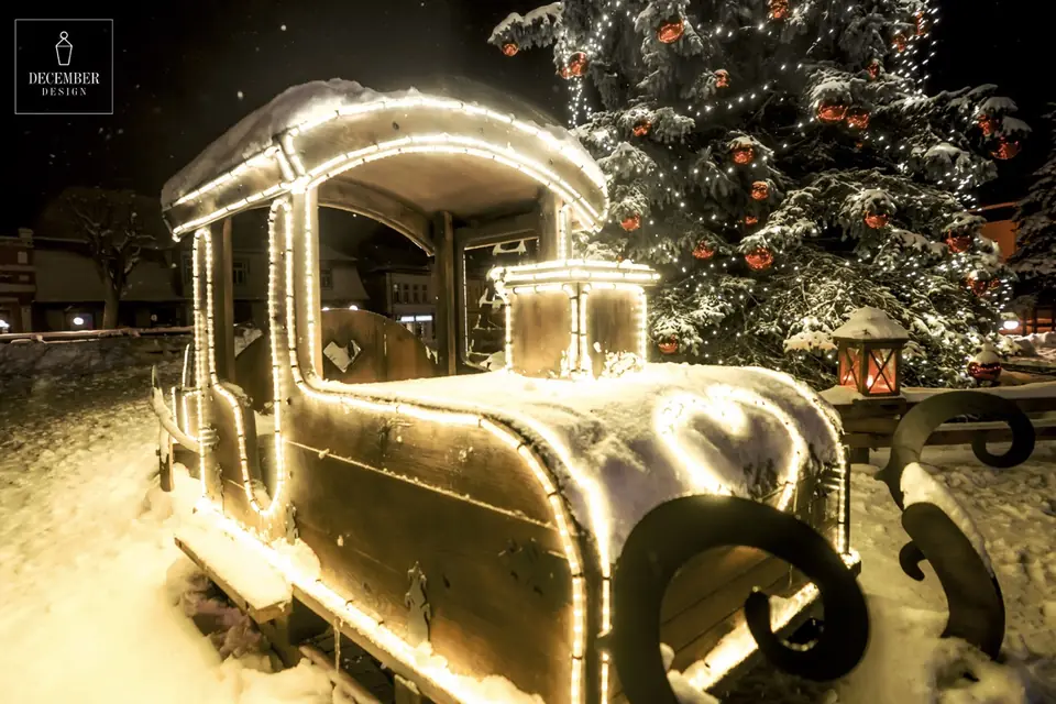 Snow covered wooden train light object with warm white outlines, behind it a fir tree with red balls