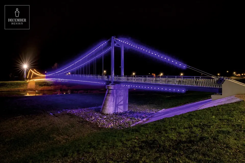 Ogre Pedestrian Bridge illuminated in purple and gold at night