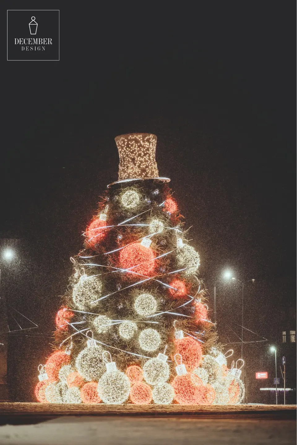 Christmas tree with spiral strings of lights, red and white balls and illuminated cylindrical top in a snowy field at night